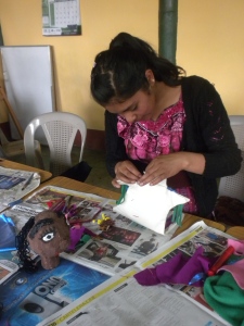 A student in Guatemala sews her puppet's body. 